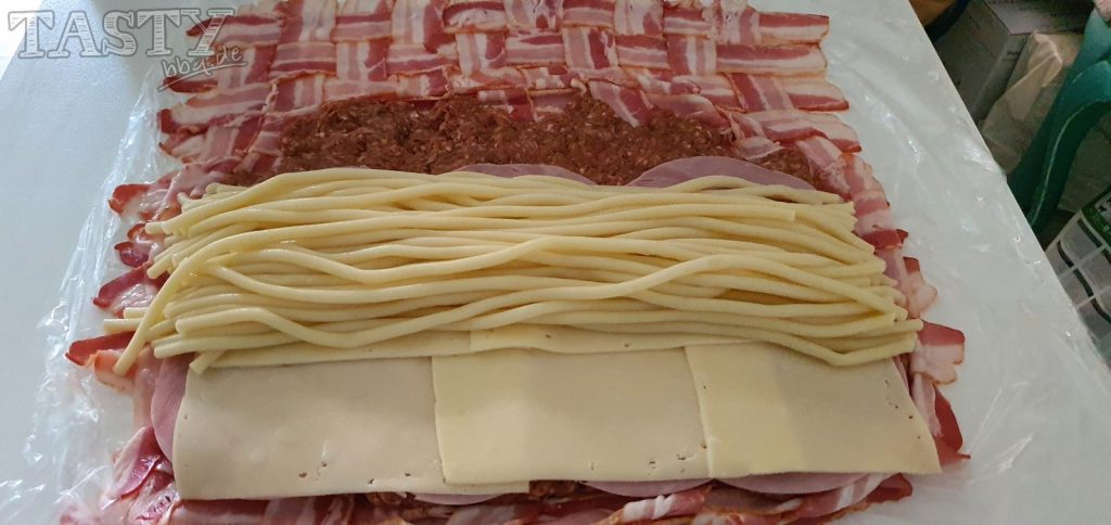 Für unsere Mac and Cheese Bacon Bomb werden jetzt auf dem Baconnetz mit dem Hackfleisch und dem Kochschinken, der Käse und die Makkaroni verteilt.